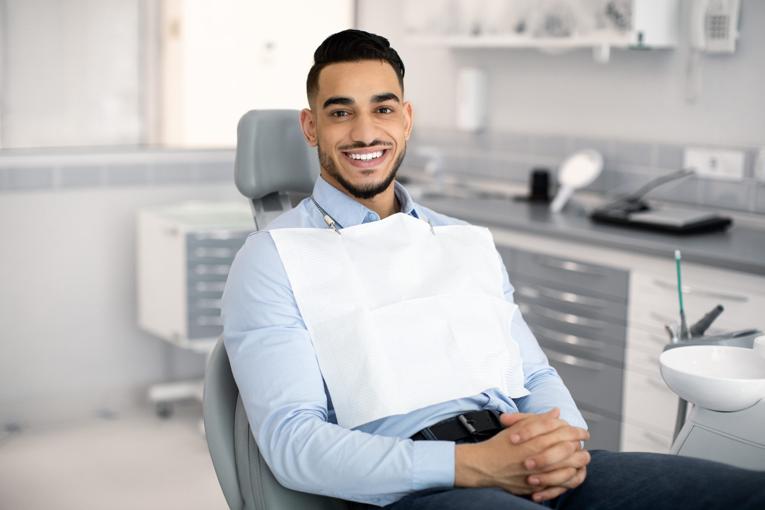 Stomatological Clinic. Portrait Of Handsome Arab Male Patient Sitting In Dentist Chair, Waiting For Check Up In Modern Cabinet, Young Middle Eastern Man Looking And Smiling At Camera, Copy Space