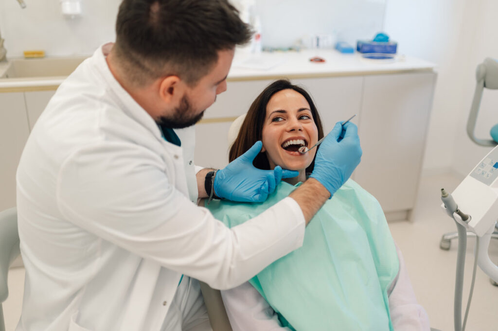 Dentist wearing gloves examines a female patient's teeth with a dental mirror and probe in a bright, modern dental clinic, ensuring her oral health